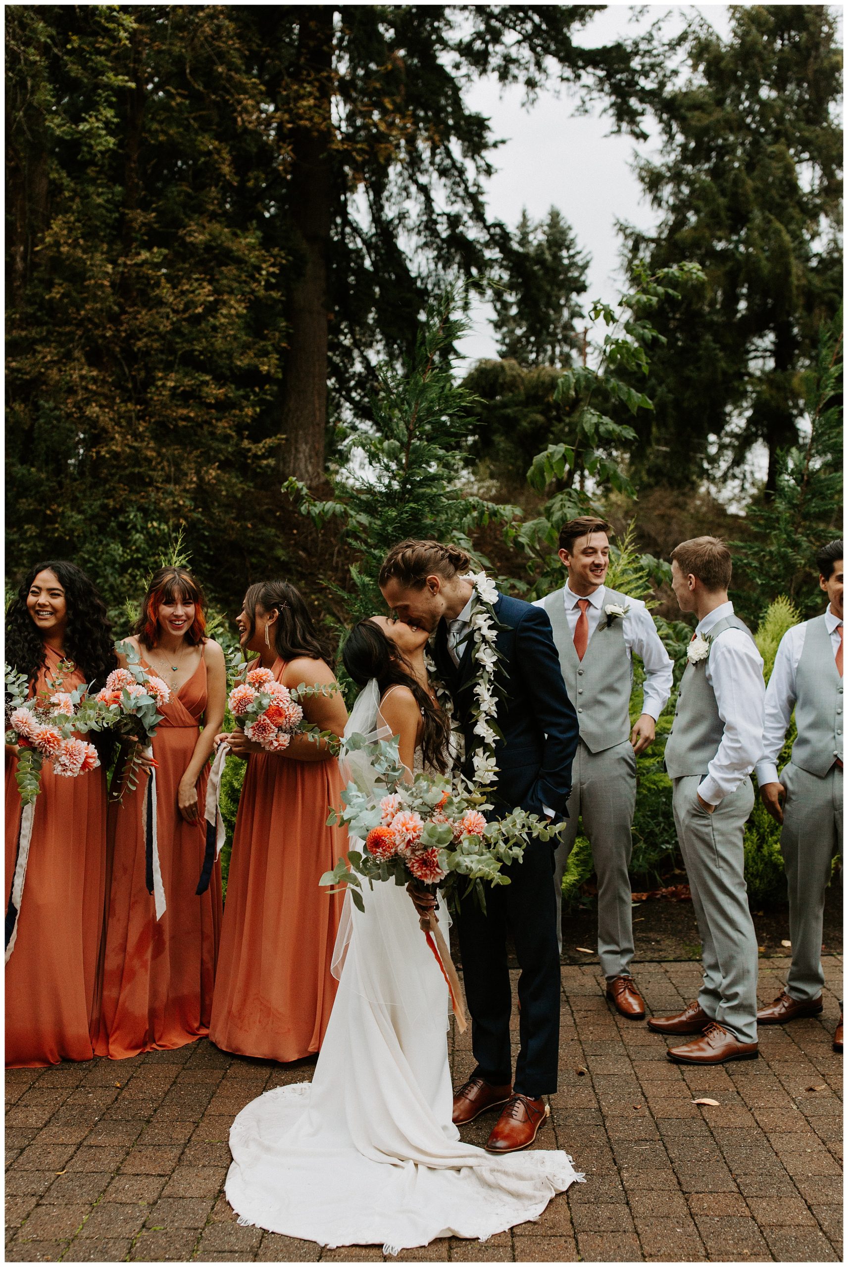 bride and groom kissing with wedding party, wedding party standing in forest
