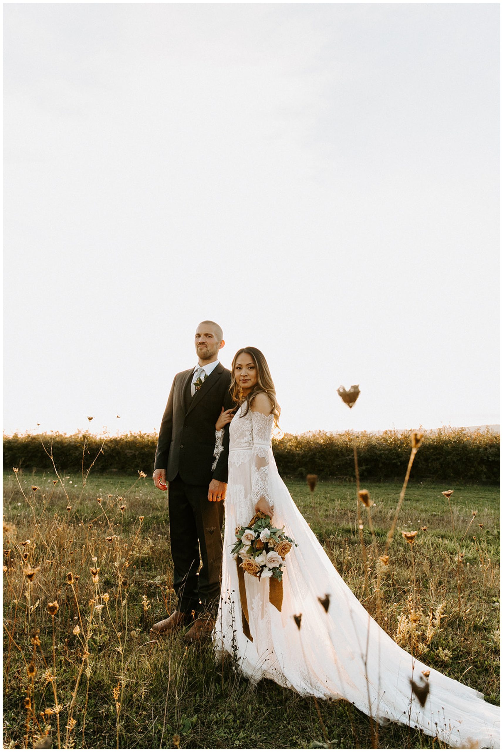 bride and groom posing in field at sunset