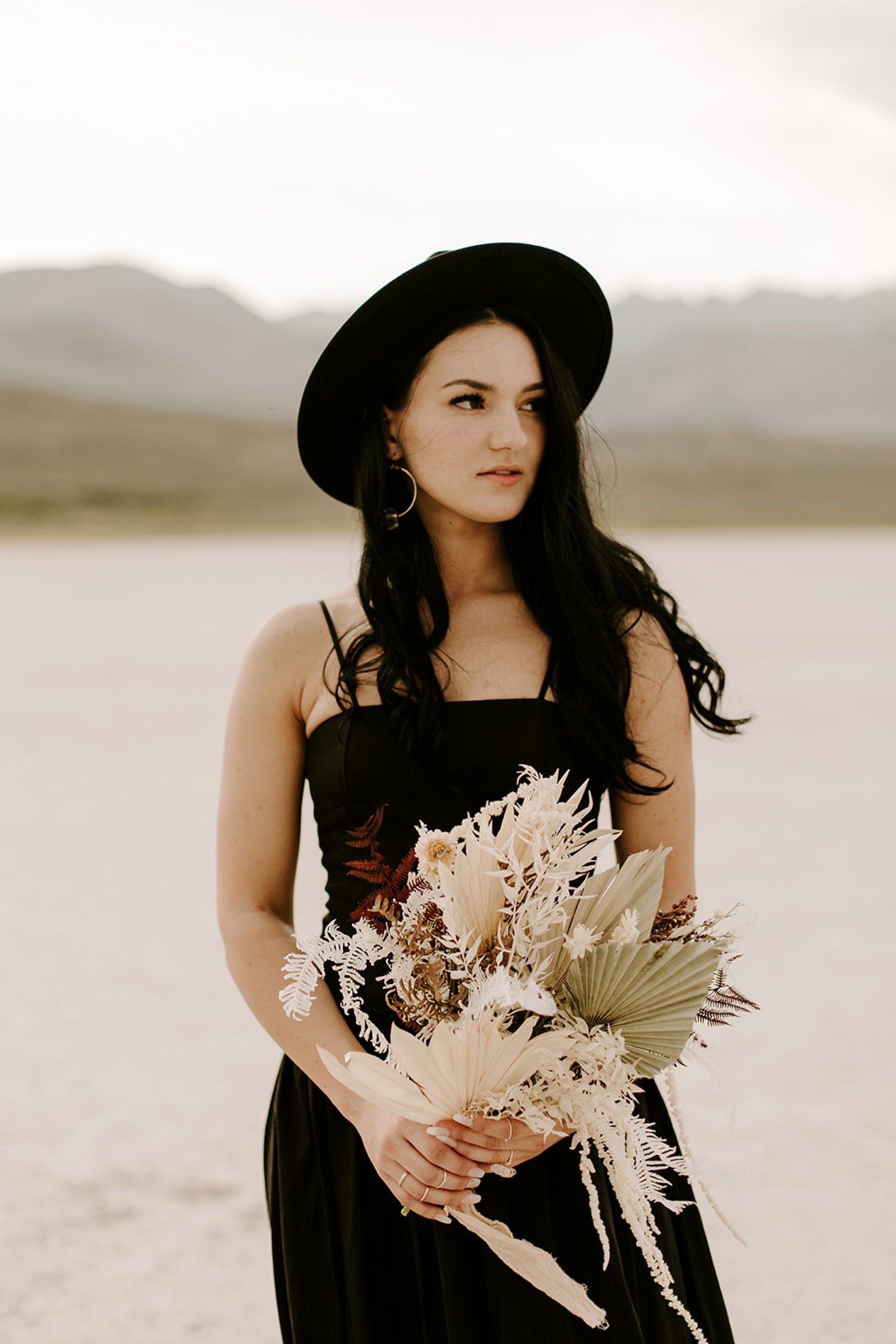 bride wearing black dress and hat holding bouquet