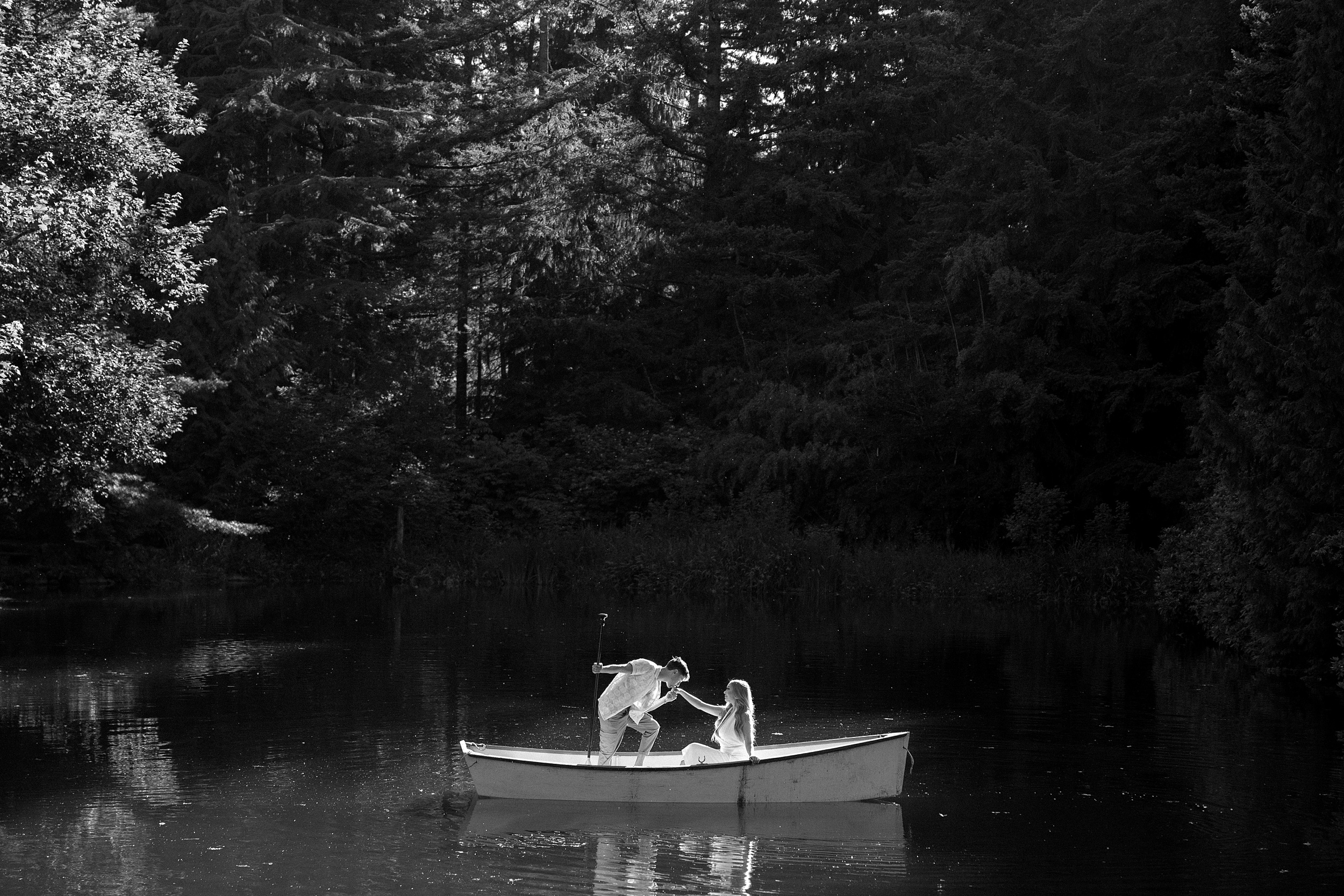 black and white picture of lake engagement photos in scenic greenery trees and a white small row boat