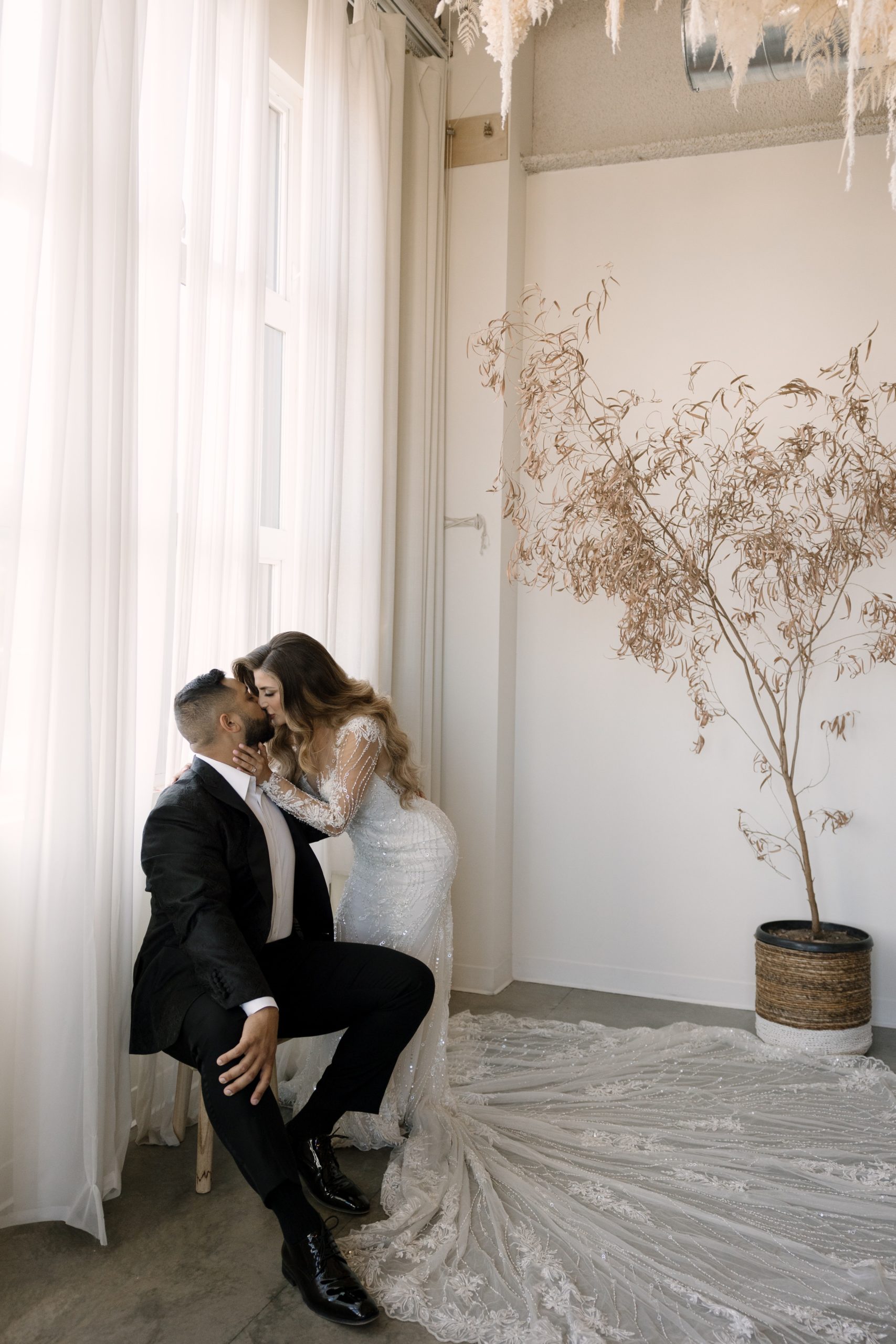 bride in white beaded maxi gown and groom in a black suite kissing at their bridal portraits