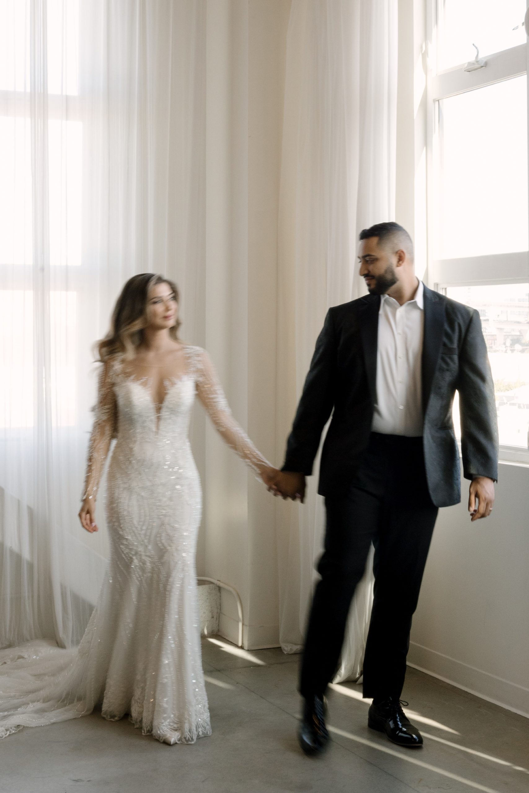 bride in white beaded maxi gown and groom in a black suite walking at their bridal portraits