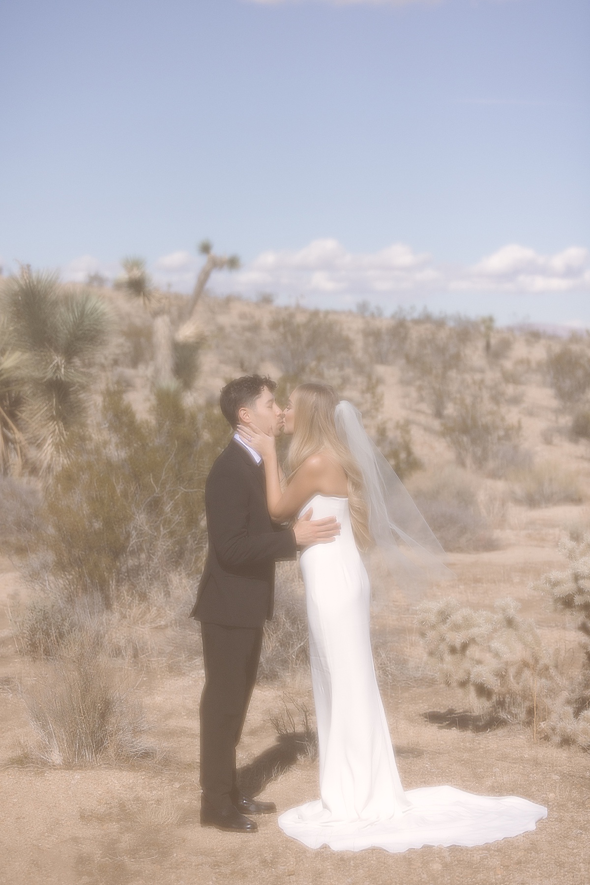 a bride in a strapless white long gown kissing her groom in an all black suit at their Joshua Tree elopement